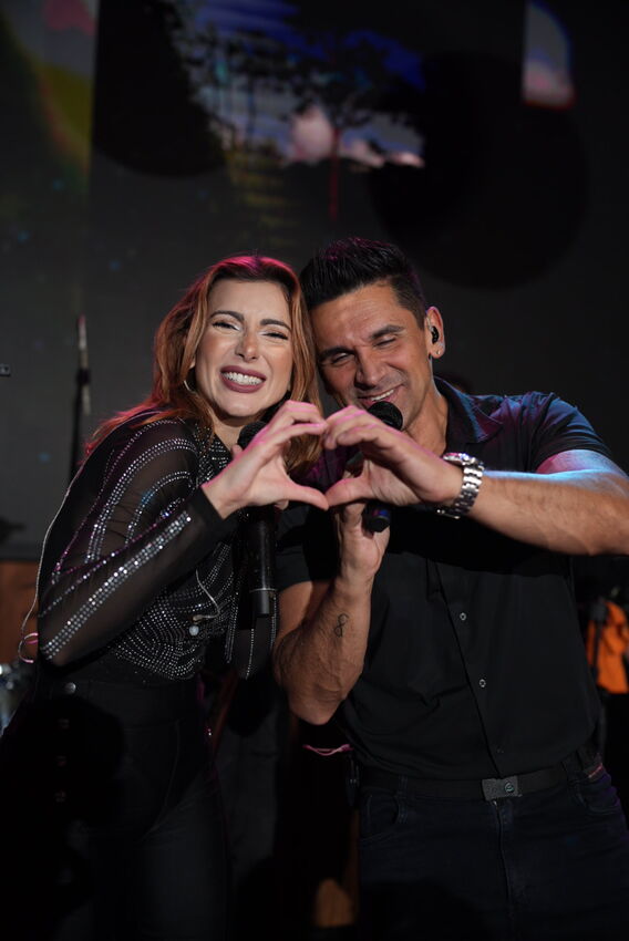 Casal de cantores da Banda iNova formando um coração com as mãos no palco
